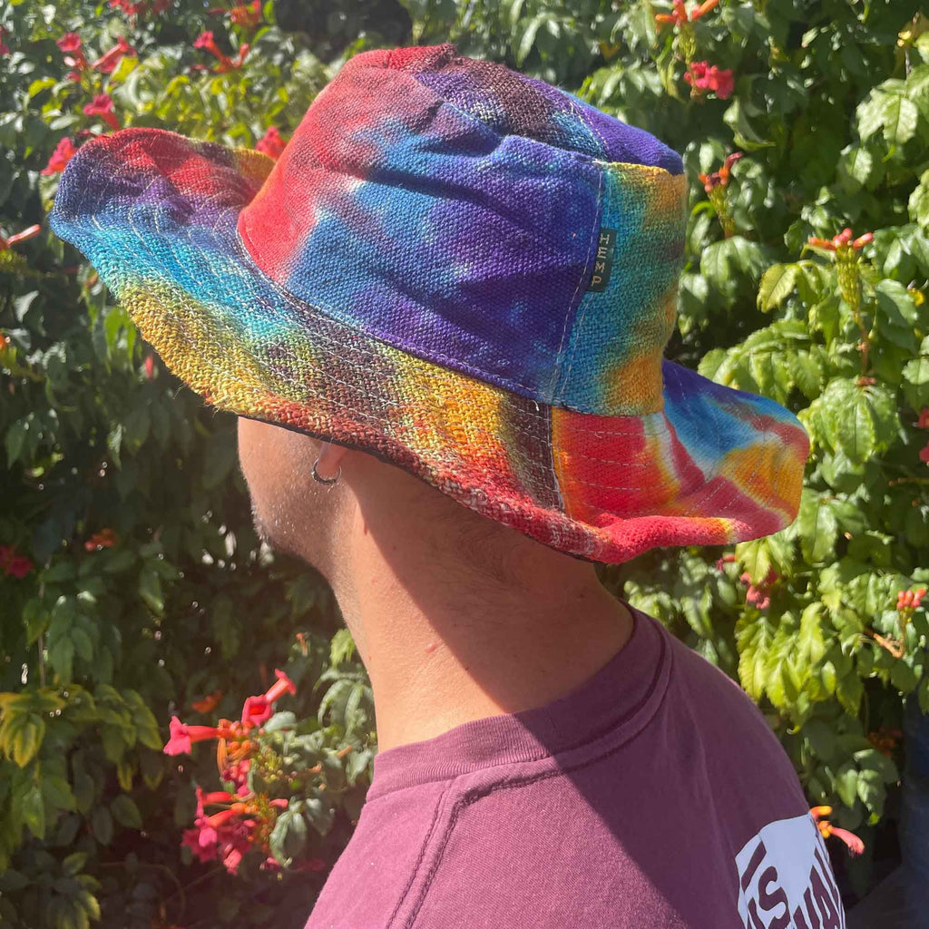 Person wearing a colorful tie-dye bucket hat with a green leafy background
